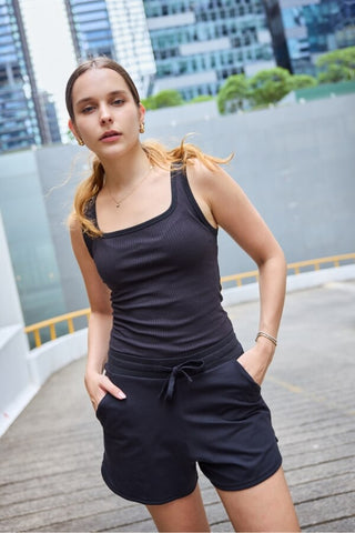 Woman wearing a black cotton tank top and shorts standing against cityscape