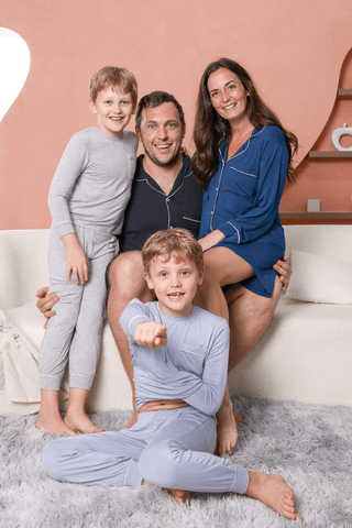 A family of four wearing matching pajamas from rawbought poses together on a white sofa in a cozy room.